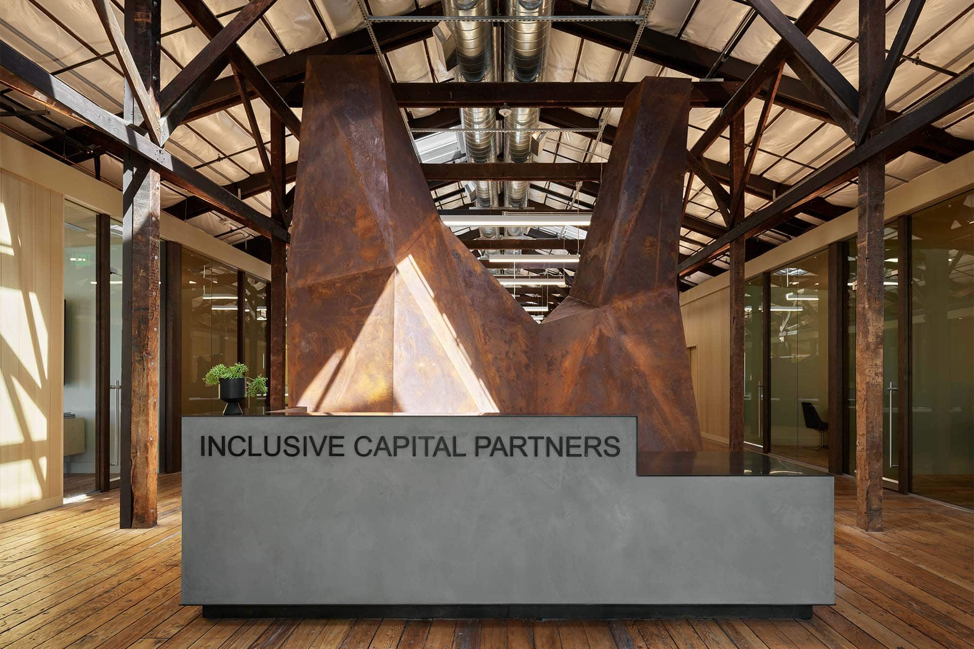 Photograph of Inclusive Capital partners office entryway displaying a custom bronze colored metal work art installation behind the front desk.
